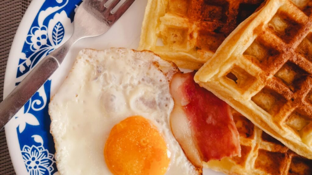 Desayuno tradicional con huevos,tocineta y waffles servidos en un plato decorativo."Cómo Ganar Dinero en Bigo Live",una opción para monetizar tu habilidad de cocinar.